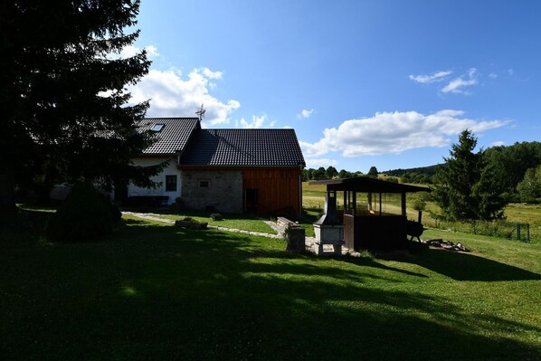 A rustic stone building with a sloped roof, a wooden structure with a chimney, and a well-maintained grassy area.