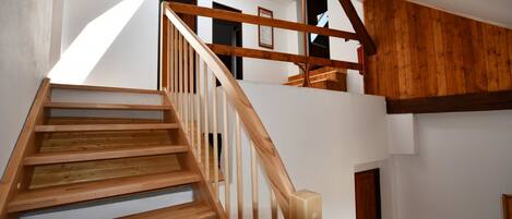 A wooden staircase leading to an upper floor with a sloped ceiling and exposed wooden beams.