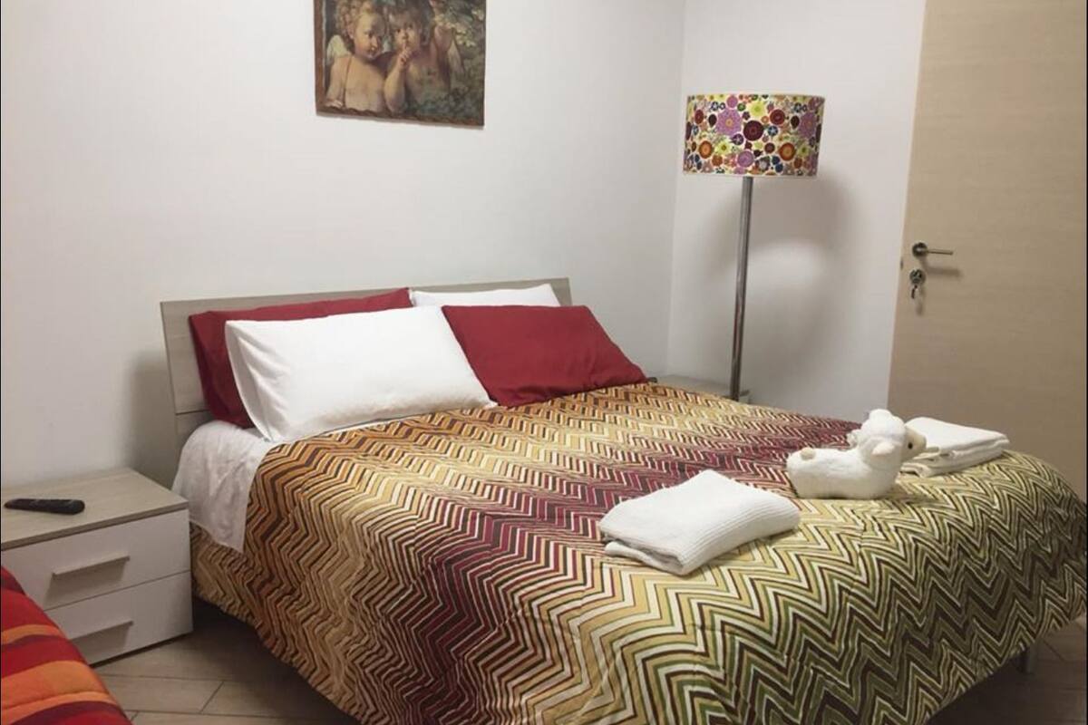 Een net opgemaakt bed met beddengoed met een patroon, een bedlampje en een schilderij aan de muur.