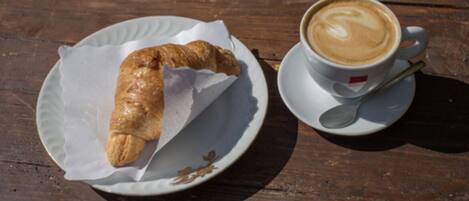 A croissant on a paper-lined plate and a cup of coffee with a spoon on a wooden table.