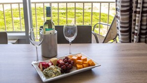 A table with a plate of cheese, grapes, and a bottle of wine, set against a view of the ocean.
