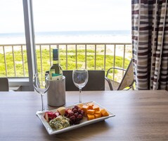 Una mesa con queso, uvas y una botella de vino, frente a una vista del océano.