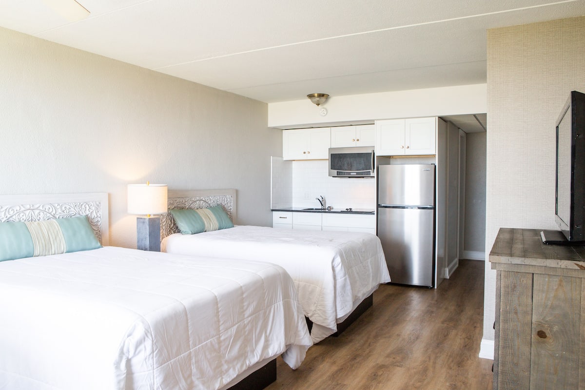 Une chambre d’hôtel avec deux lits, une kitchenette et un téléviseur.