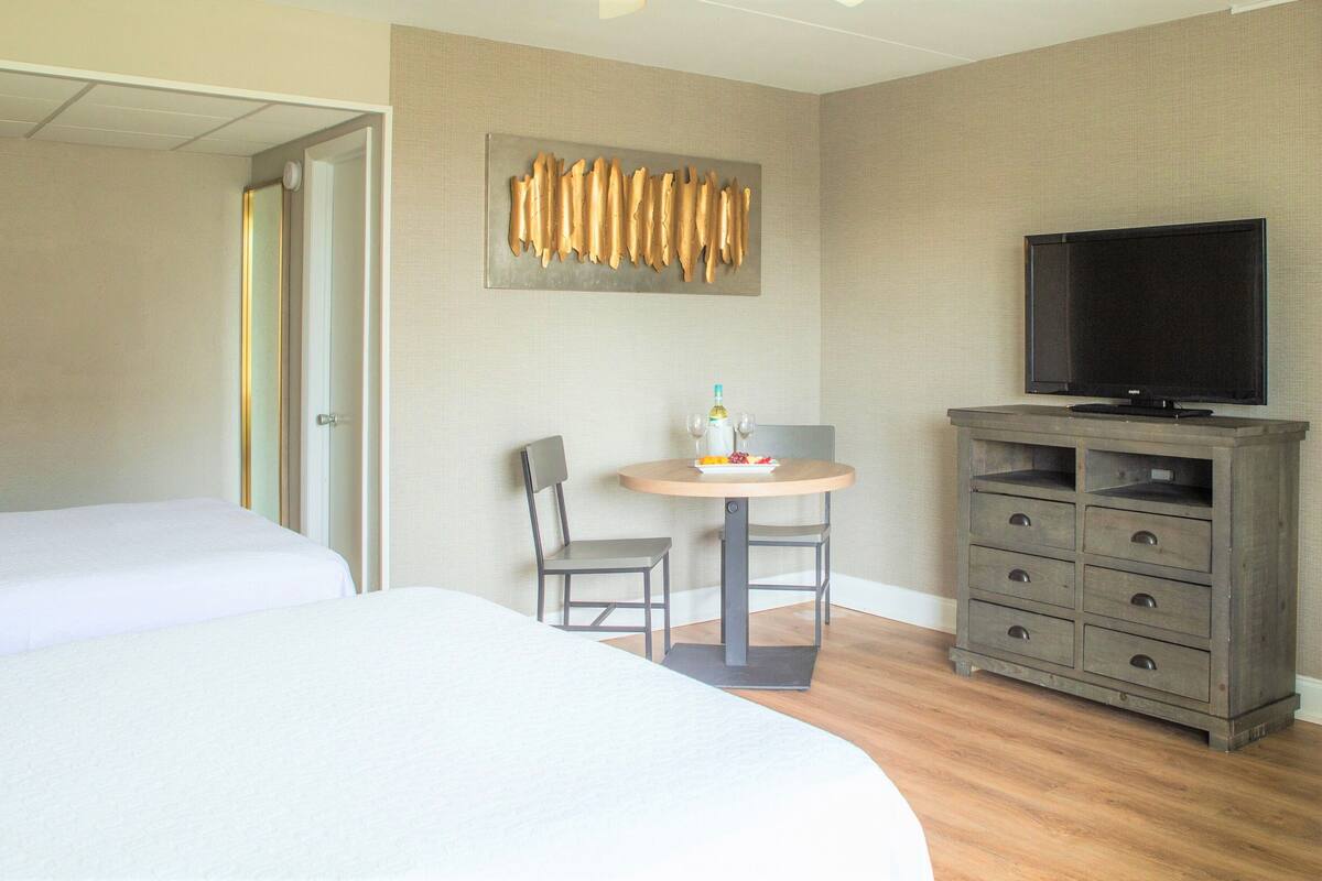 Une chambre d’hôtel avec un grand lit, une télévision, une petite table avec une bouteille et des verres, et une chaise.