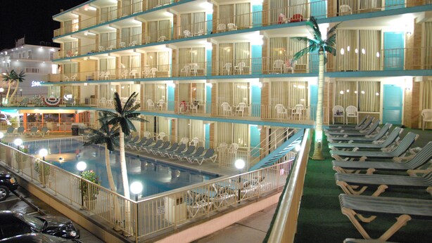 A multi-story hotel with a swimming pool, balconies with chairs, and a beachside view.