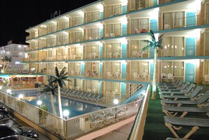Un hotel de varios pisos con piscina, balcones con sillas y vista al mar.