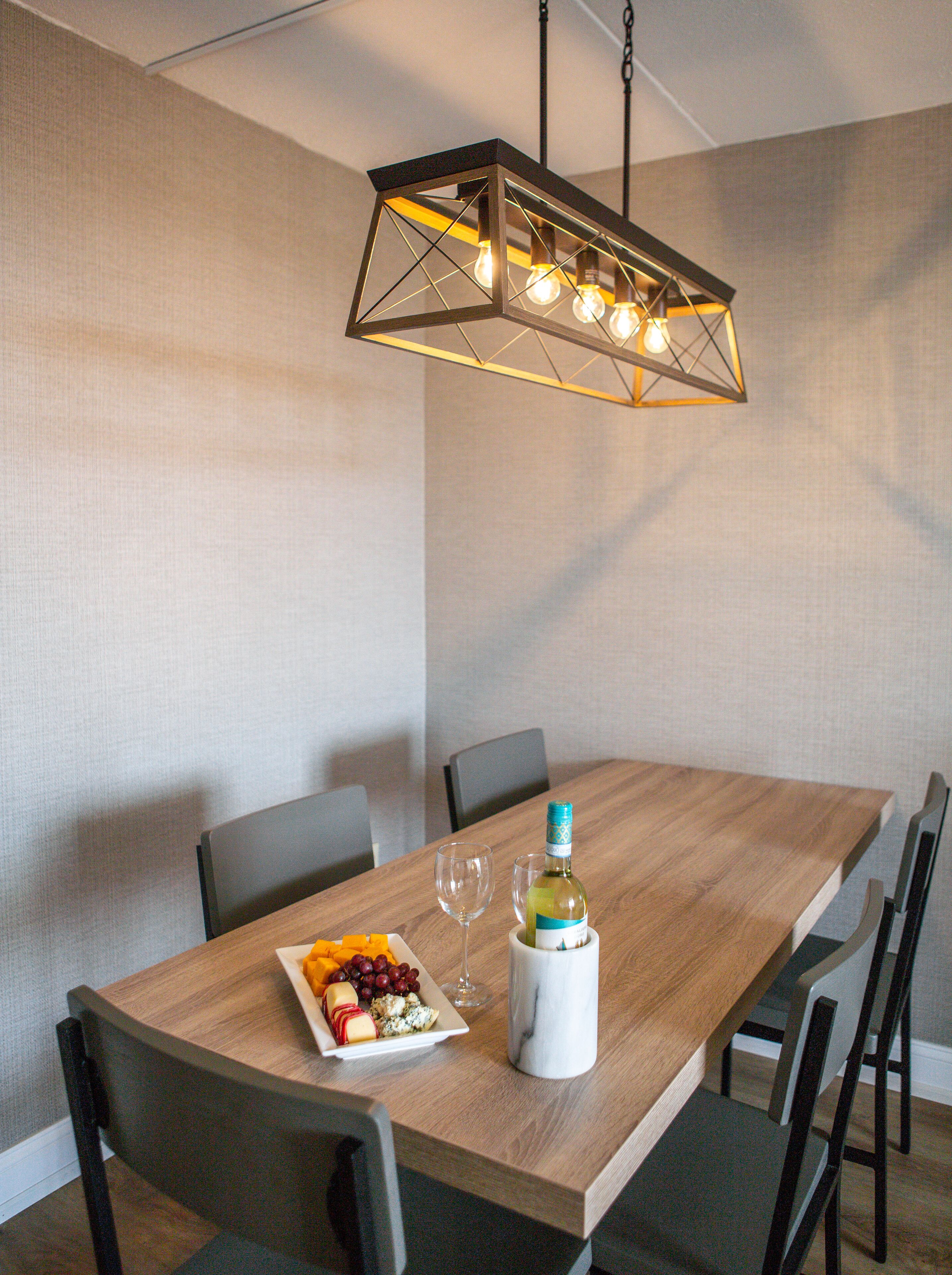 Un coin repas avec une table en bois, des chaises, un verre à vin, une bouteille de vin et une assiette de fromage et de raisins.