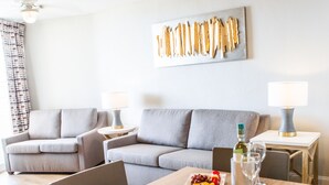 A modern living room with two grey sofas, a wooden dining table with a fruit platter, wine glasses, and a bottle.