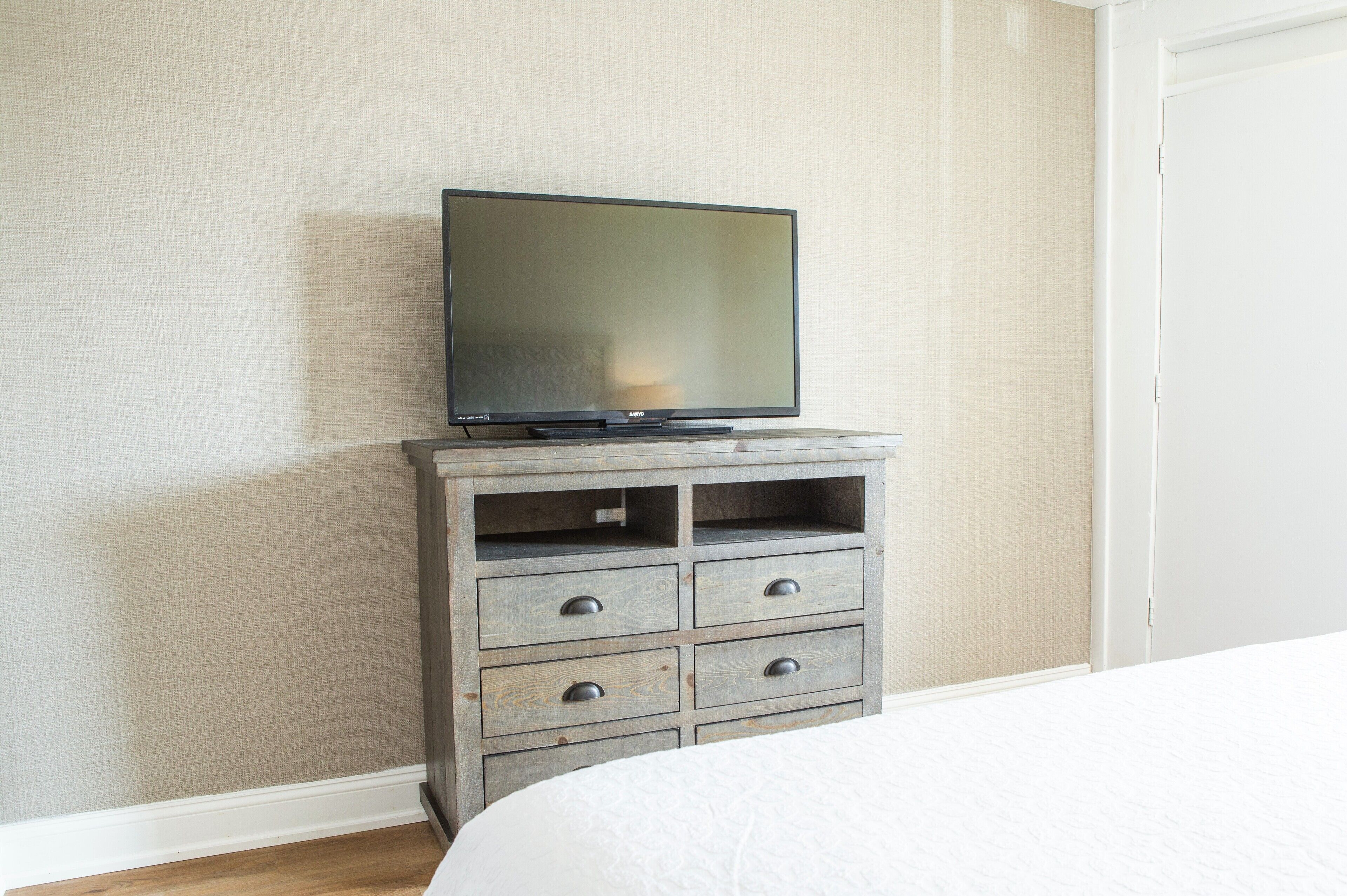 Un dormitorio con una cama, un televisor sobre un aparador de madera y una pared lisa.