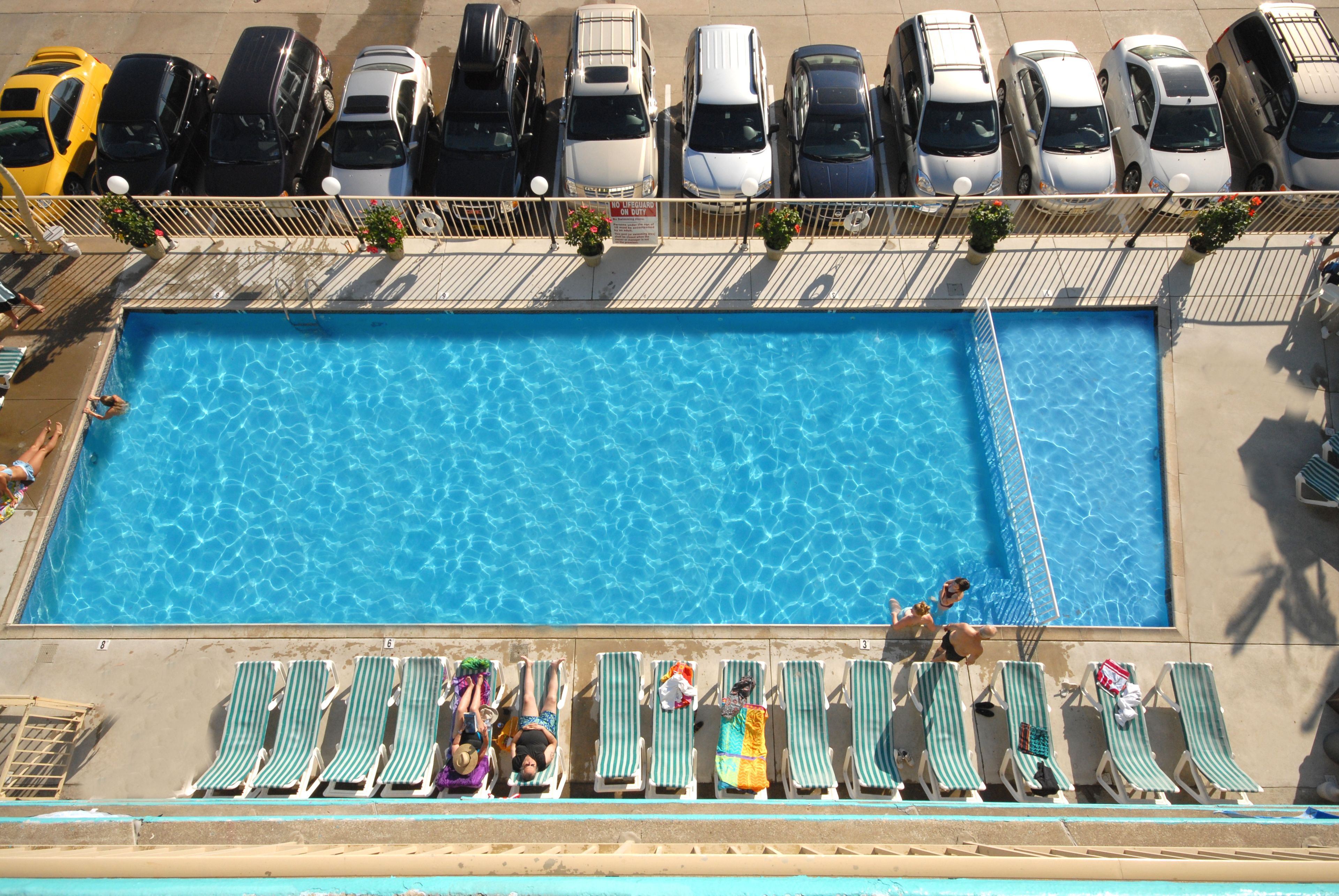 A swimming pool with lounge chairs and a parking area with cars.