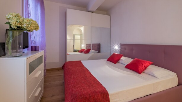 A modern bedroom with a bed, a dresser, a mirror, and a vase with flowers.