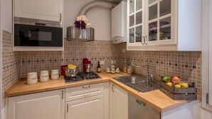 A kitchen with white cabinets, a stainless steel oven, a gas stove, and a sink. There are jars on the counter and a fruit basket.