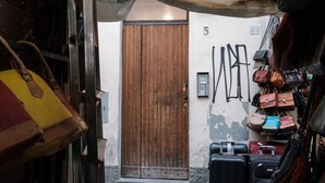 A narrow alley with a wooden door, numbered 5 and 23, and a wall with hanging bags.