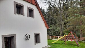 A house with a white exterior, three windows, and a swing set in the yard. - Chalupa Jiřík (Volary)