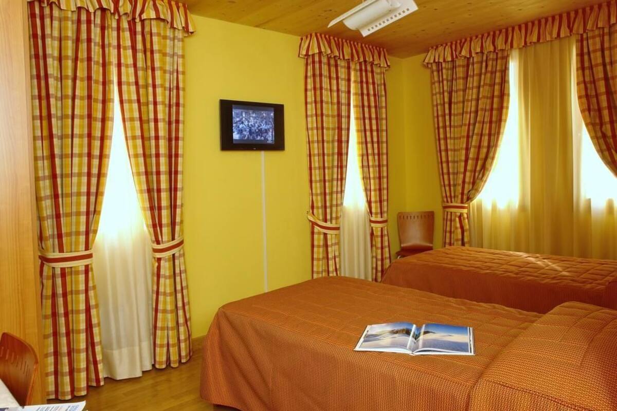 A room with two beds, checkered curtains, a framed picture on the wall, and a book on one bed.