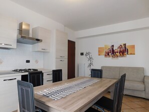 Een moderne keuken met witte kastjes, een gasfornuis en een eethoek met een houten tafel en stoelen.