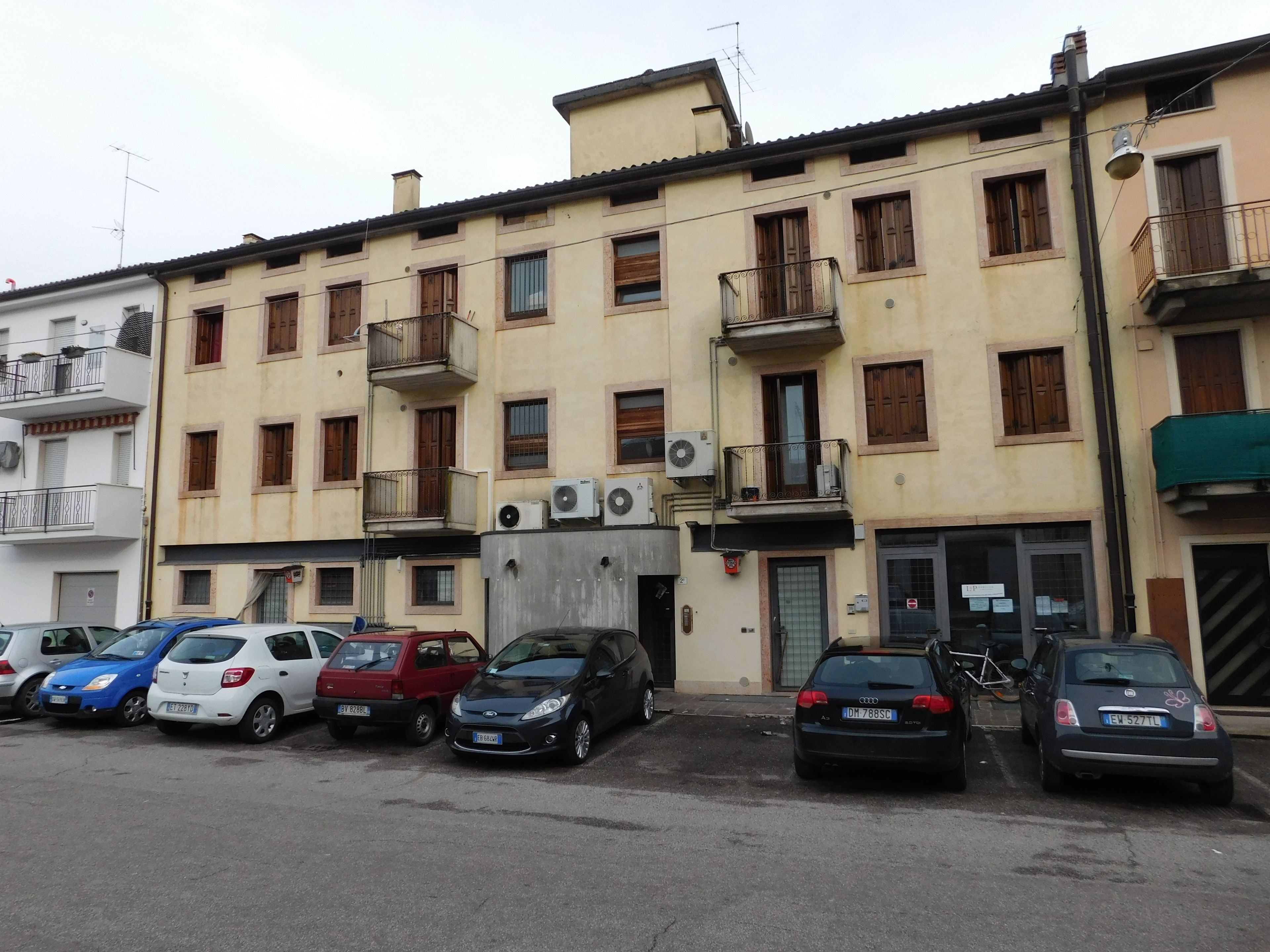 Fila di auto parcheggiate di fronte a un edificio con numerosi balconi e finestre.