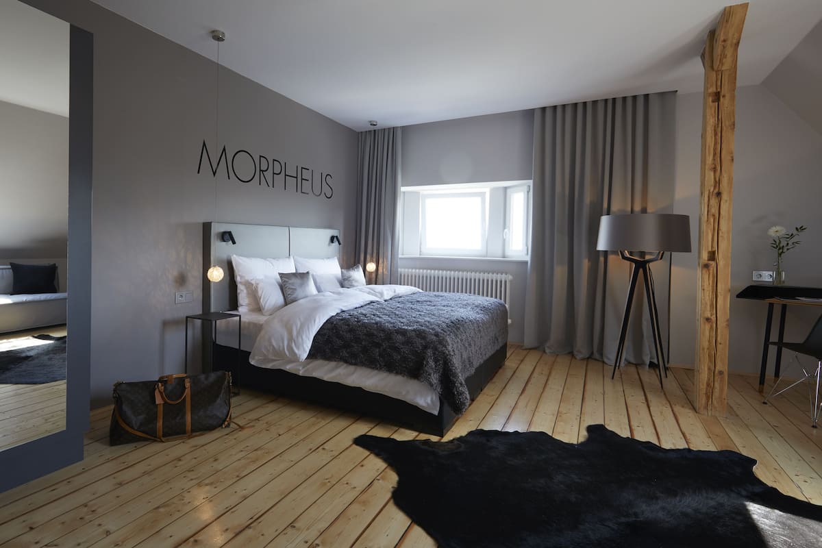 A modern bedroom with a bed, a nightstand, a lamp, a wooden floor, and a black fur rug.
