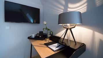 Ein moderner Schreibtisch mit einem Flachbildfernseher, einer Lampe, einer Vase mit einer weißen Blume und einem Notizblock.