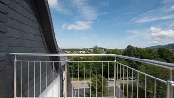 A balcony with a metal railing overlooking a residential area with trees and houses.