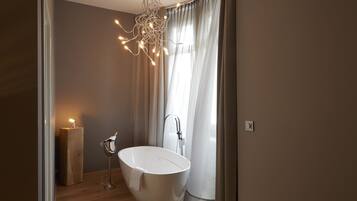 A modern bathroom with a freestanding bathtub, a wooden side table with a candle, and a unique chandelier.