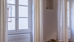 A room with a large window, a radiator, a wooden table with a vase and a book, and stone arches on the ceiling. - Parione Apartment (Florence)