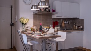 A modern kitchen with white cabinets, a wooden dining table, and pendant lights. - Parione Apartment (Florence)