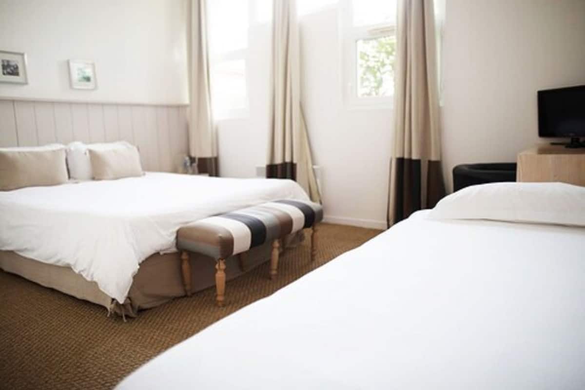 A hotel room with two beds, a flat-screen TV, and a window with curtains.
