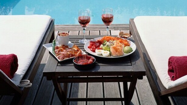 A wooden table with a meal and two glasses of red wine, set between two lounge chairs by a pool. - La Maison de la Prade (Messanges)