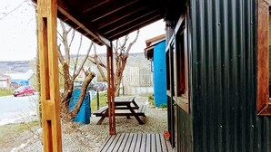 Un patio in legno coperto che conduce a un edificio in metallo ondulato, con tavolo da picnic e panche.