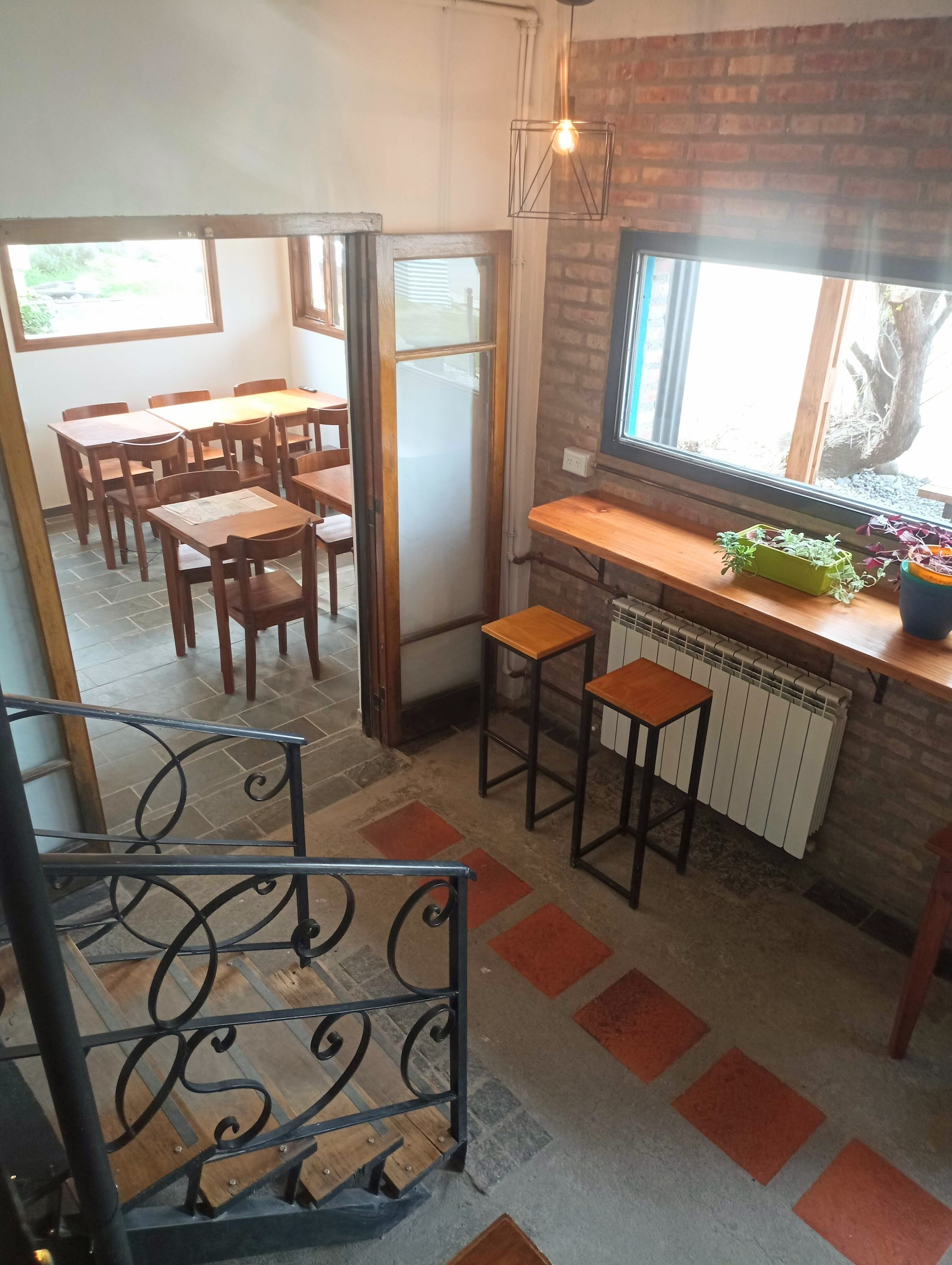 Een gezellig eetgedeelte met houten tafels en stoelen, een bakstenen muur en een raam met planten.