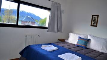 A bedroom with a bed, a window with a view of mountains, a radiator, and a framed picture on the wall.