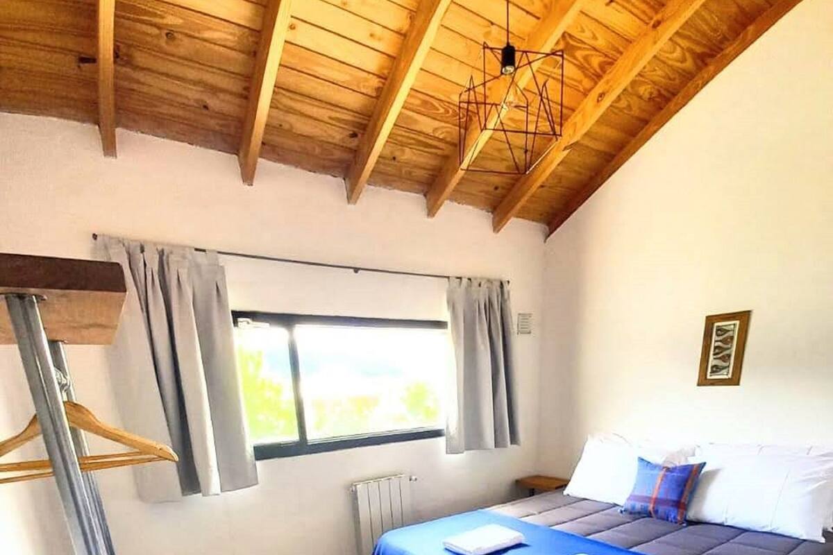 Un dormitorio con una cama litera, techo de madera, ventana con cortinas y un radiador.