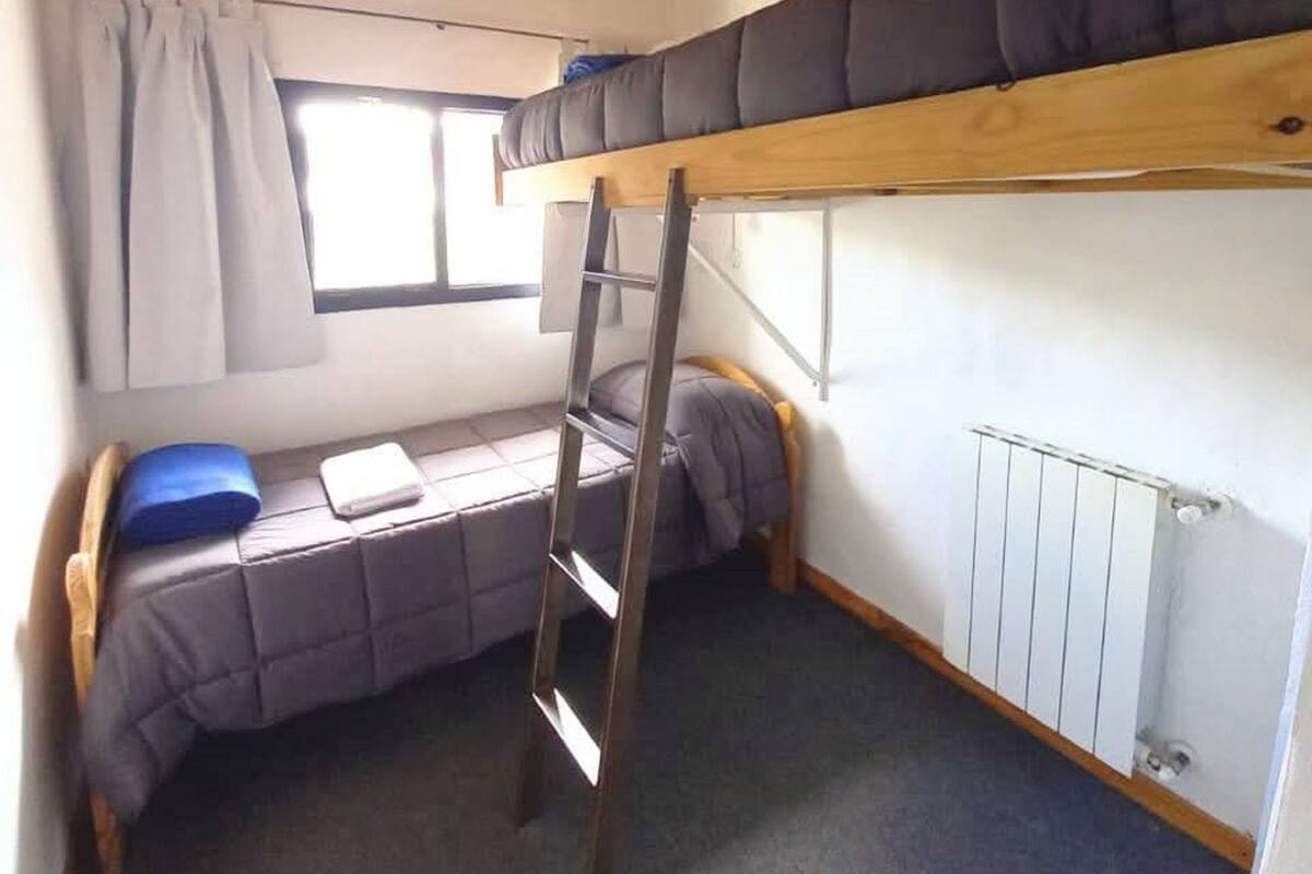 Habitación con literas, una escalera, una ventana con cortinas y un radiador.