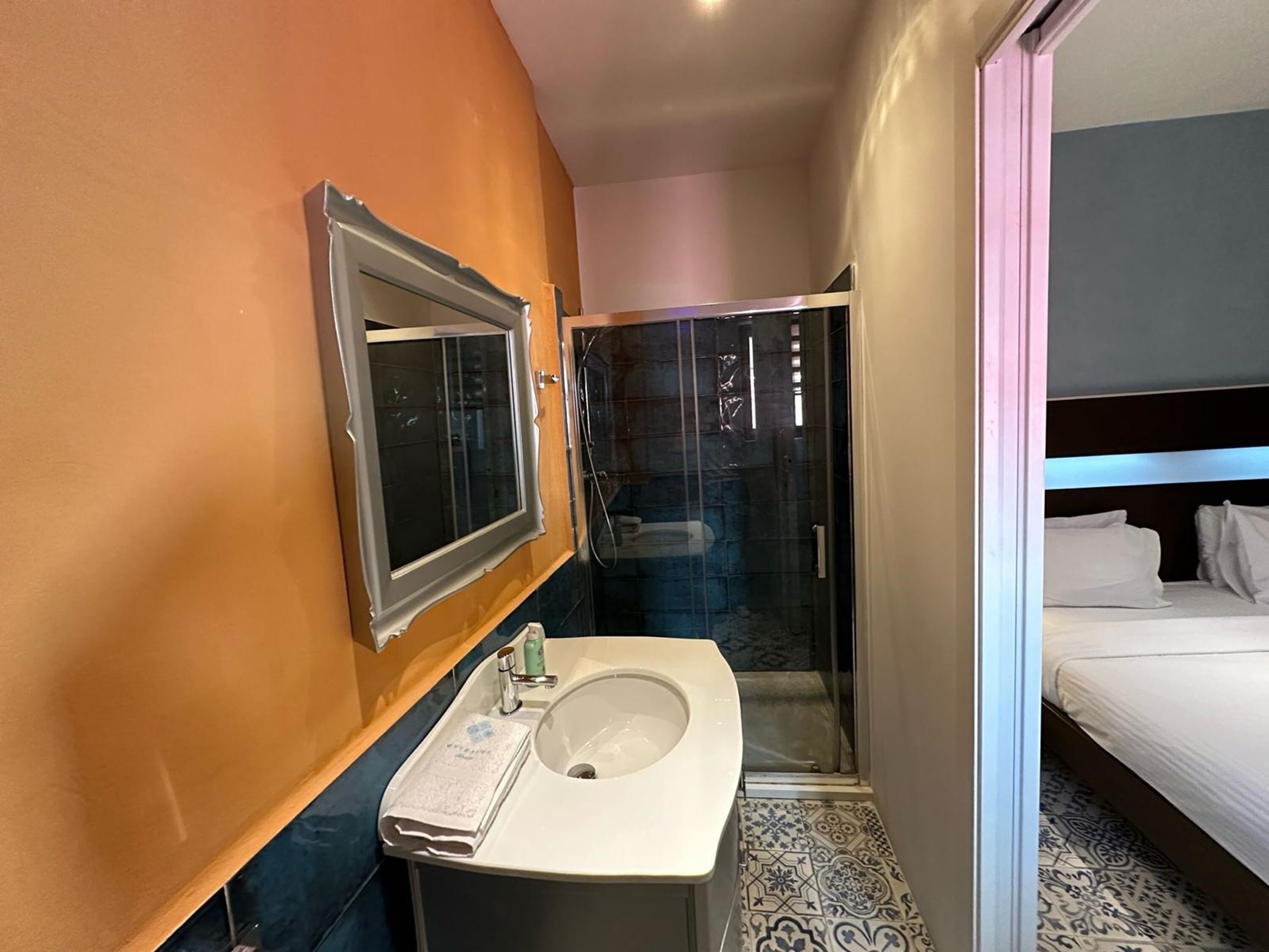 Habitación de hotel pequeña con baño que incluye lavamanos, espejo y ducha.