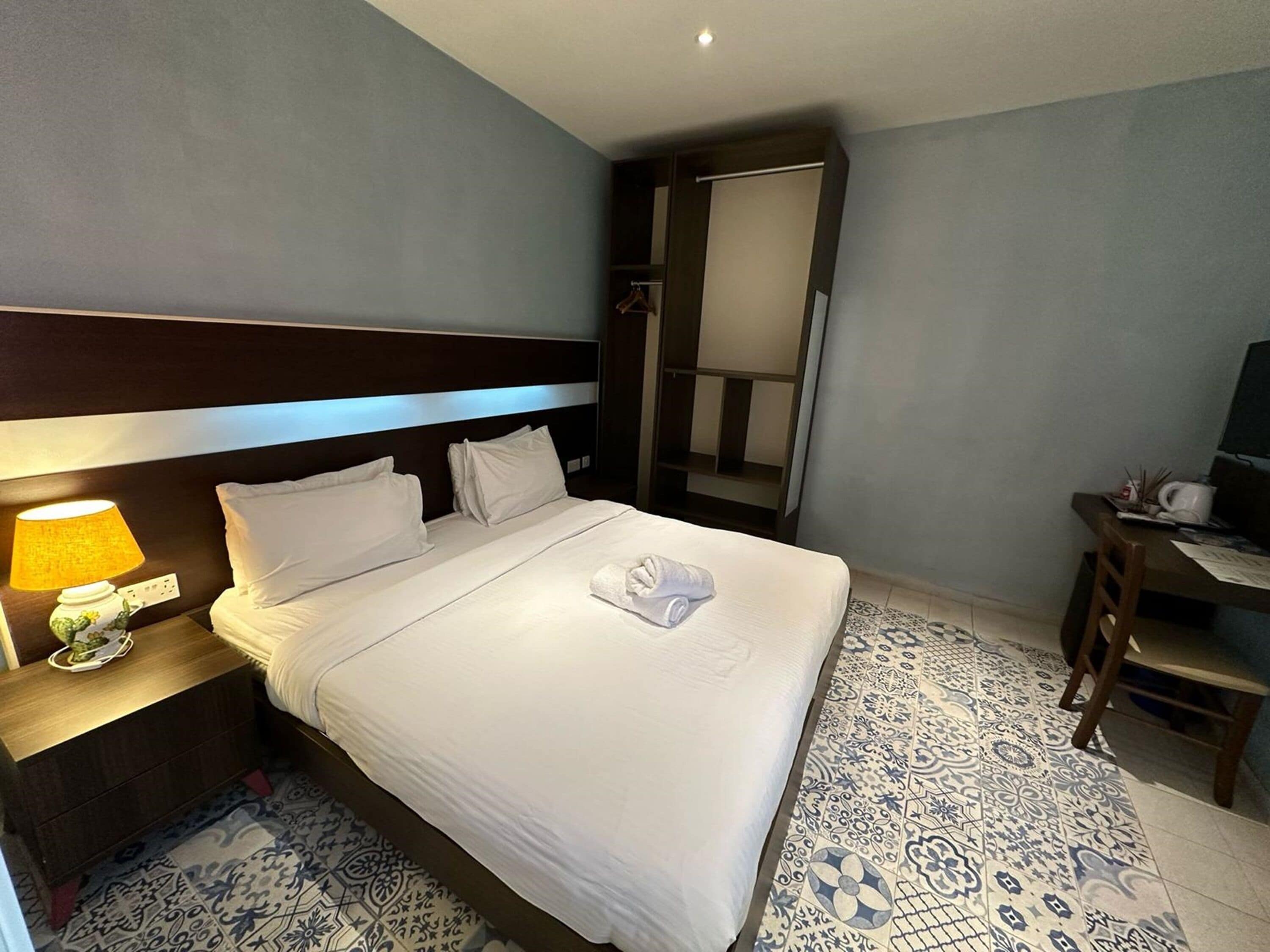 Una habitación de hotel con una cama bien hecha, una lámpara de noche, un escritorio con silla y un espejo grande.