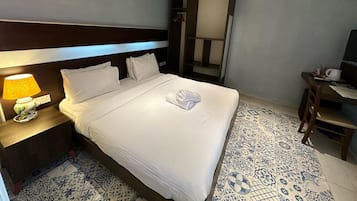 Una habitación de hotel con una cama bien hecha, una lámpara de noche, un escritorio con silla y un espejo grande.
