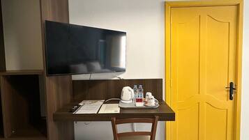 A small room with a wooden desk, a television mounted on the wall, a yellow door, and patterned floor tiles.