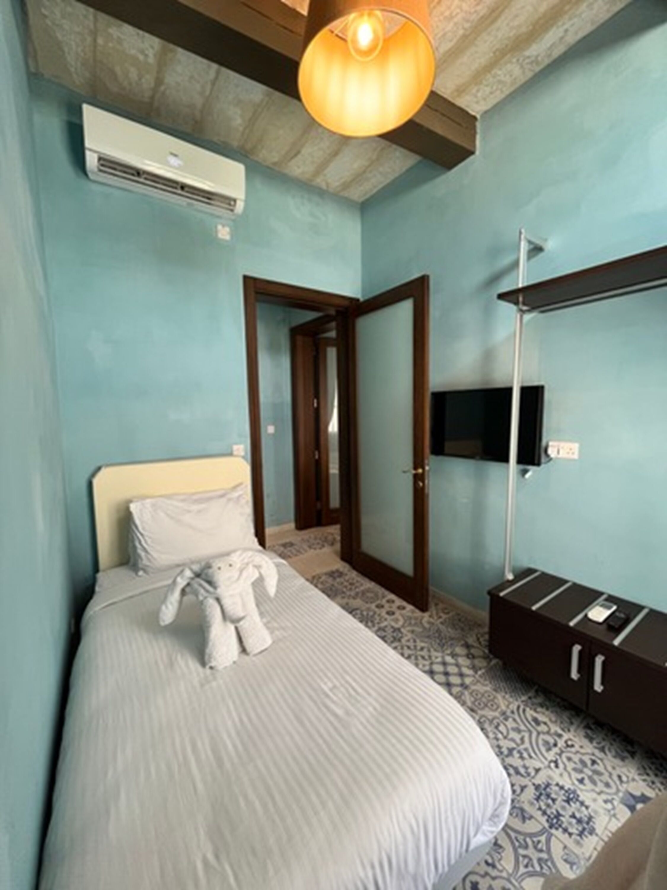 A bedroom with a bed, a bedside lamp, a TV mounted on the wall, and a wardrobe.