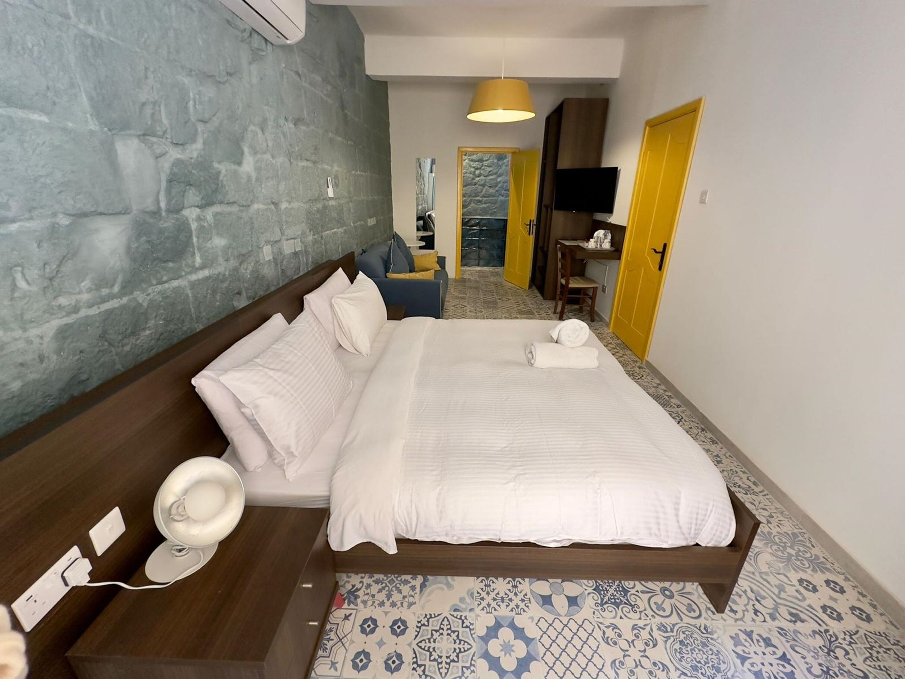 Ein Hotelzimmer mit einem großen Bett, einem Nachttisch mit Lampe, einem Fernseher und einem Schreibtisch mit Stuhl.
