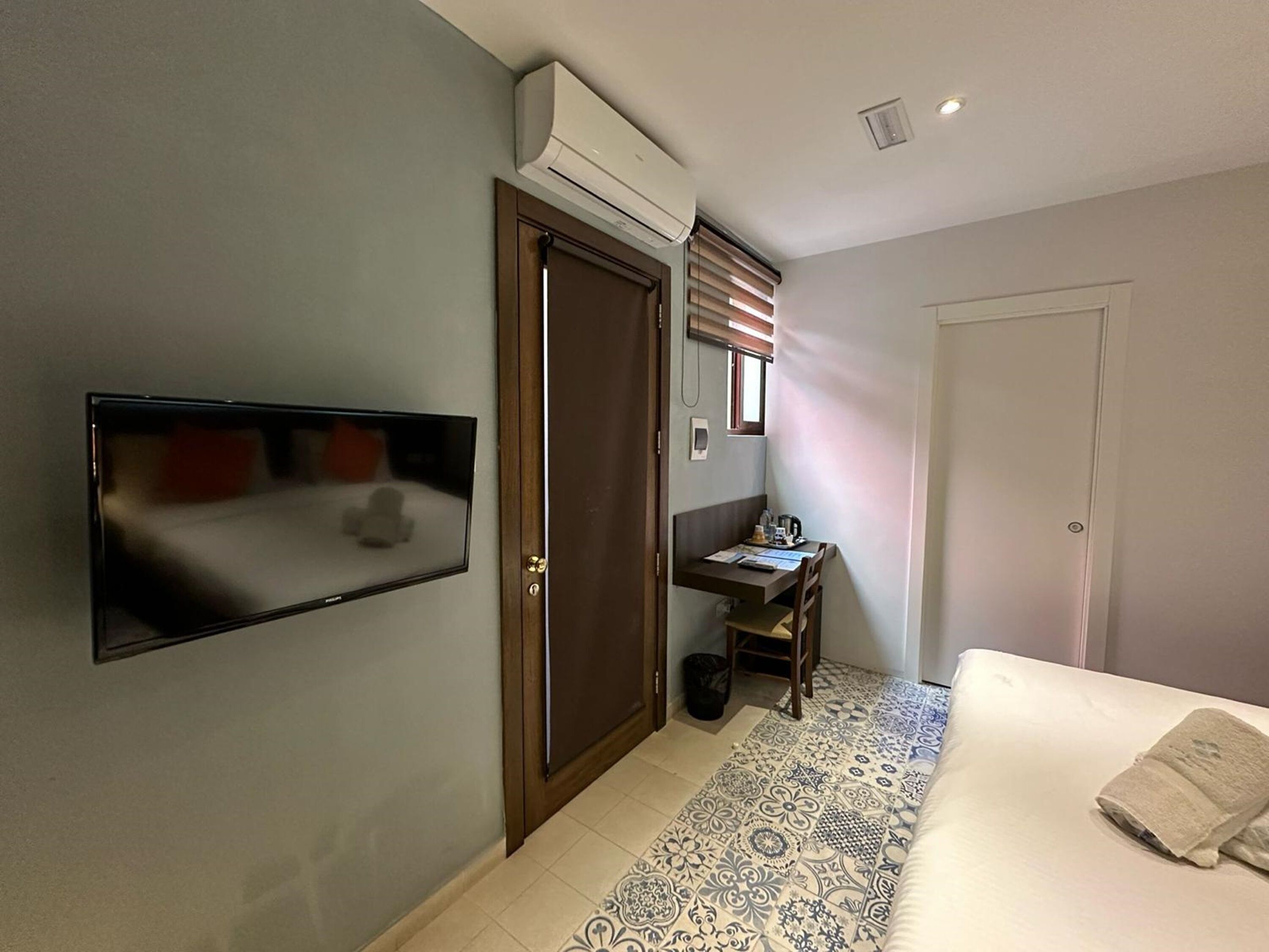 Een hotelkamer met een bed, een bureau, een televisie en een airconditioning.