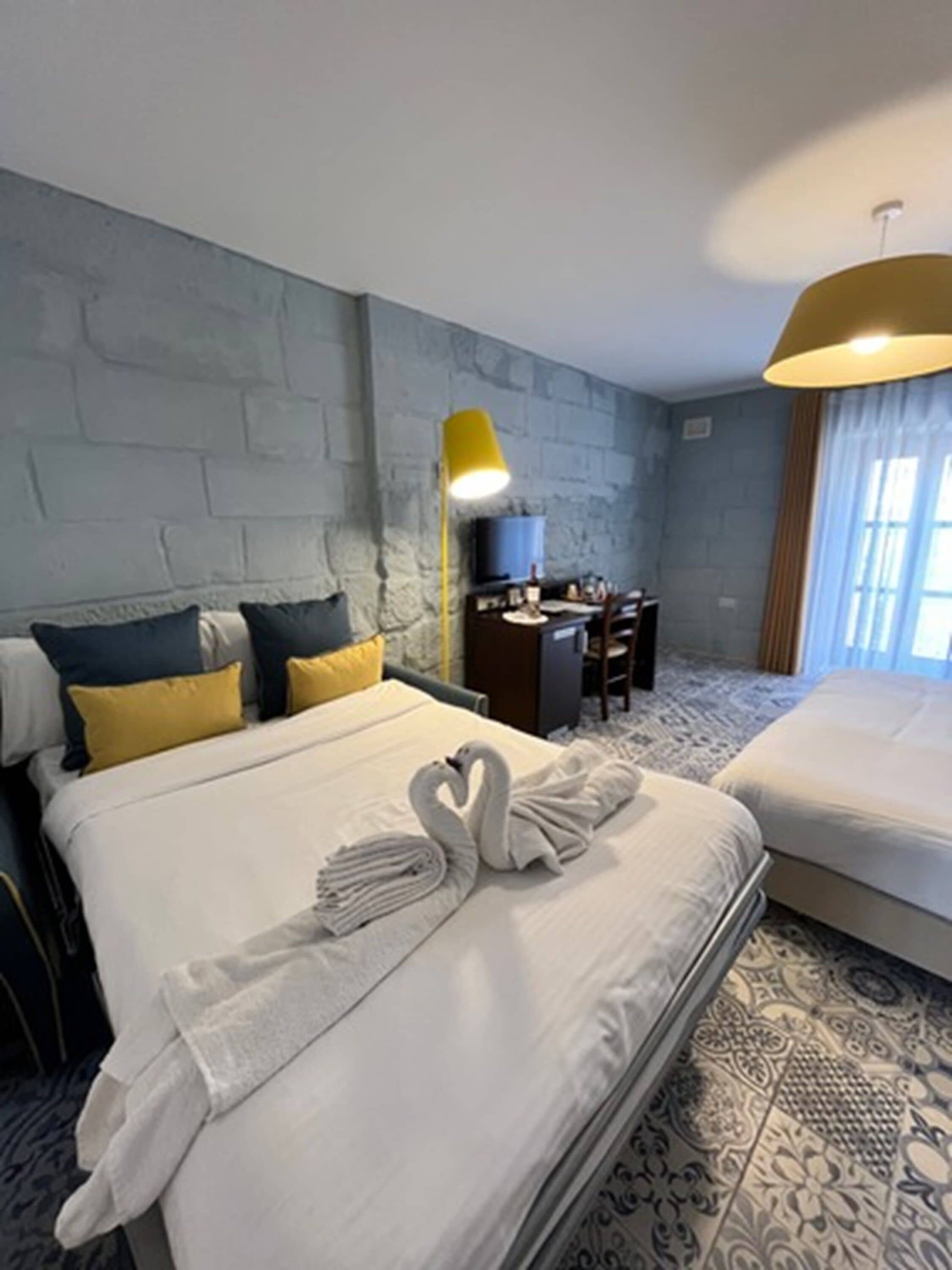 A hotel room with a large bed, a desk with a chair, a lamp, and a TV.