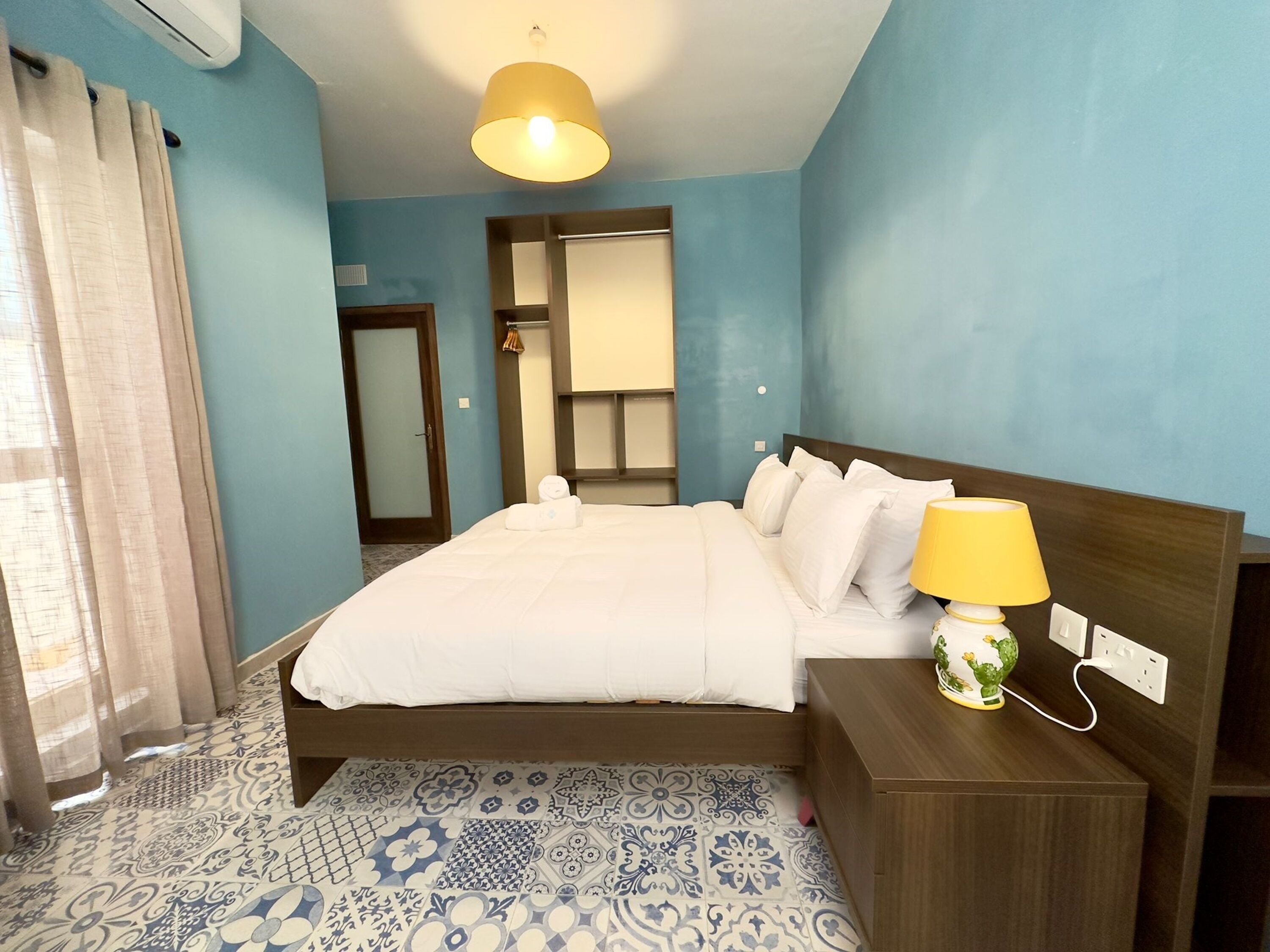 Una habitación de hotel con cama, mesita de noche, lámpara y suelo estampado.