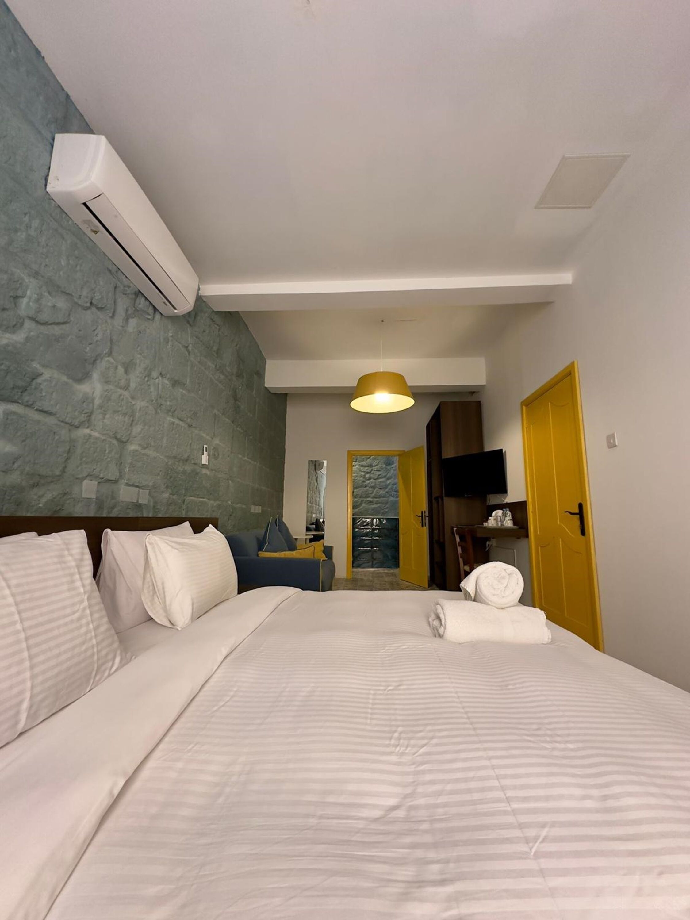 Quarto de hotel com cama, sofá, ar condicionado fixado na parede, luminária de teto e porta.