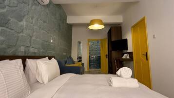 Quarto de hotel com cama, sofá, ar condicionado fixado na parede, luminária de teto e porta.