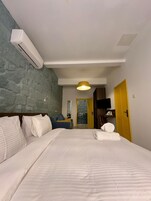 Quarto de hotel com cama, sofá, ar condicionado fixado na parede, luminária de teto e porta.