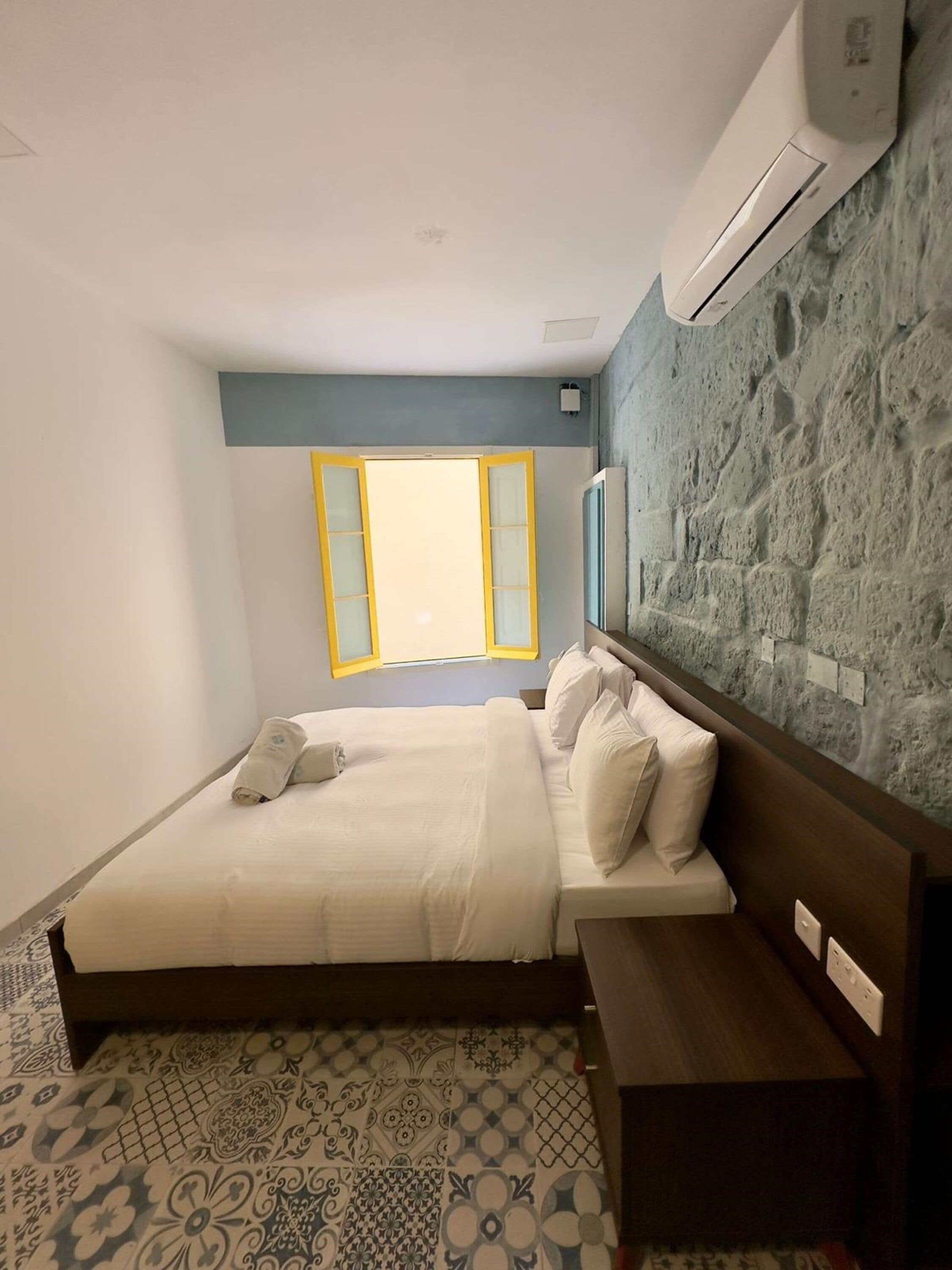 Ein Schlafzimmer mit Bett, Nachttisch und Fenster mit gelben Rahmen.
