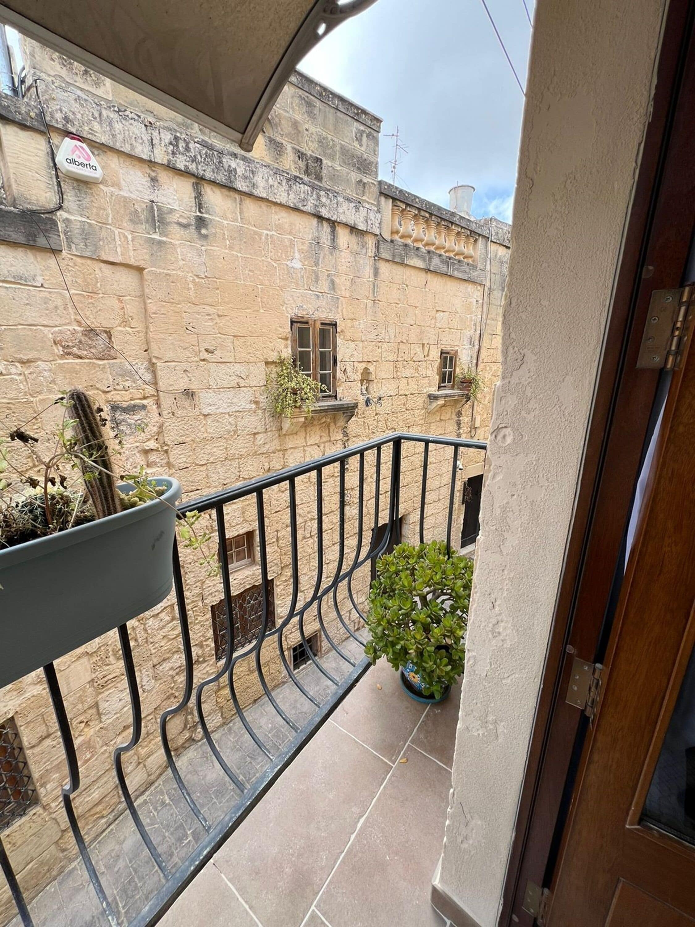 Un balcon donnant sur un bâtiment en pierre, avec une plante en pot et une rambarde en métal.