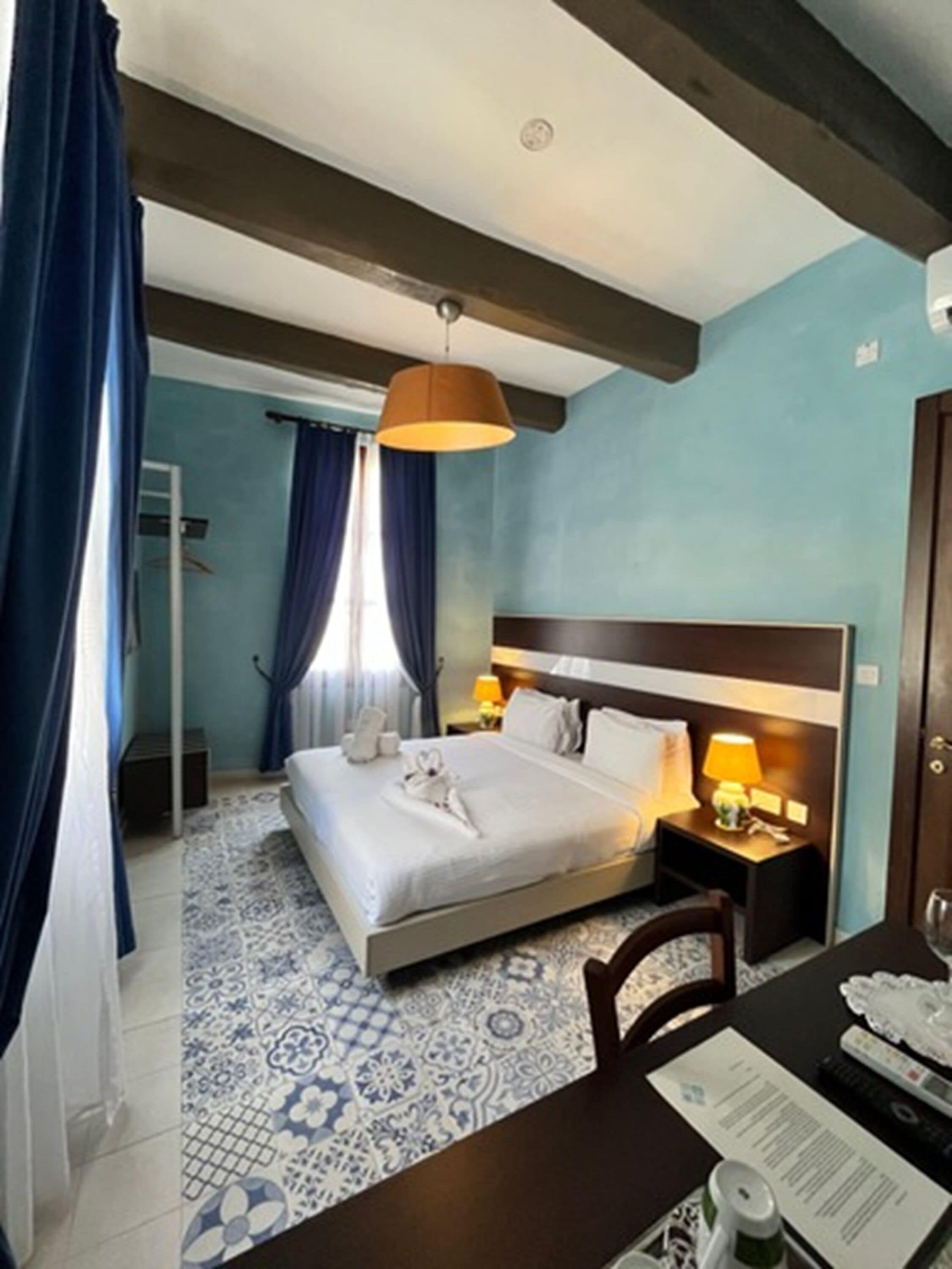 A hotel room with a bed, bedside table, lamp, and a blue patterned rug.