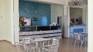 A modern bar area with a blue backsplash, metal chairs, and a chandelier. - Hotel Moja (Cesenatico)